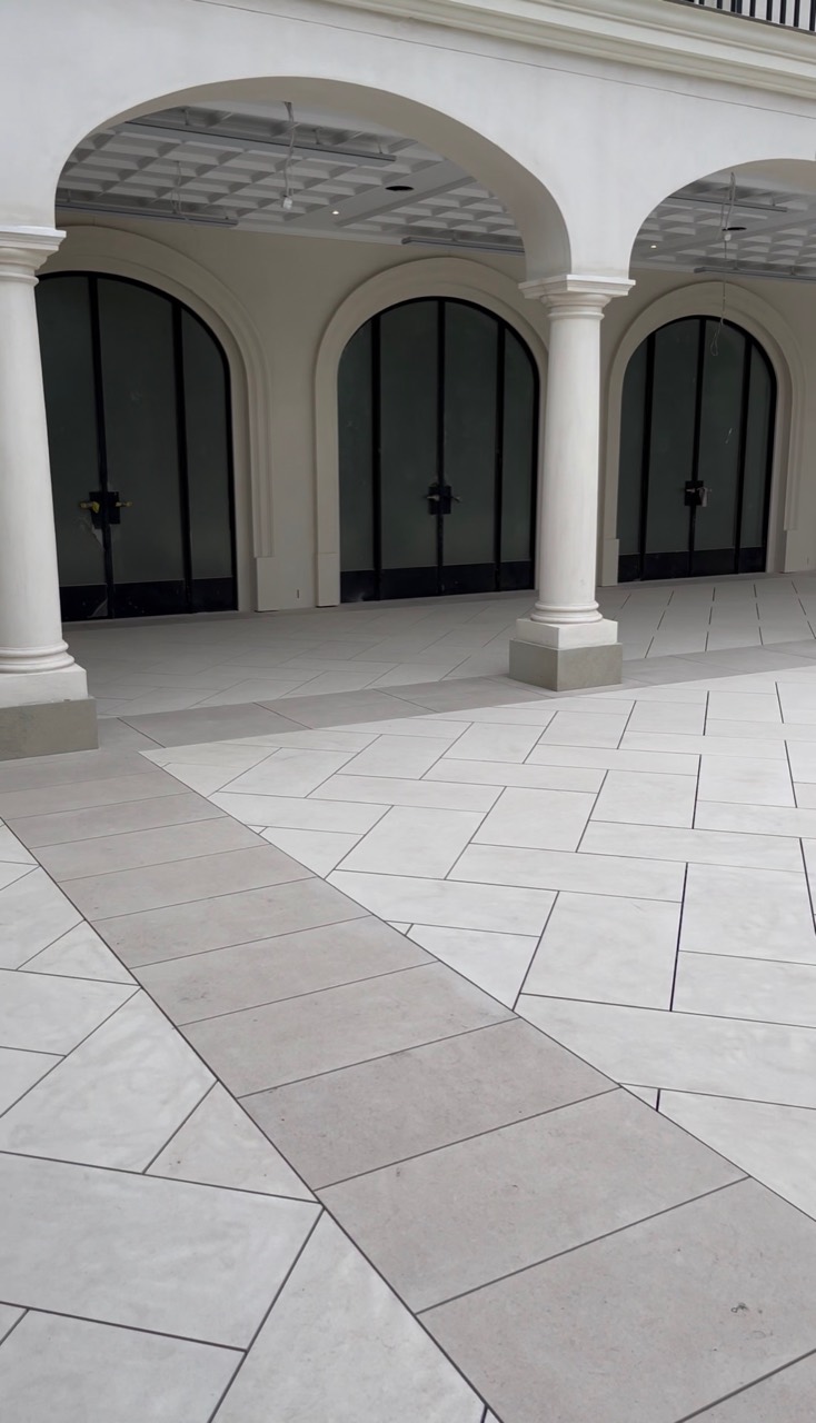 Large-format pale stone tiles laid in a geometric courtyard pattern beneath classical arches