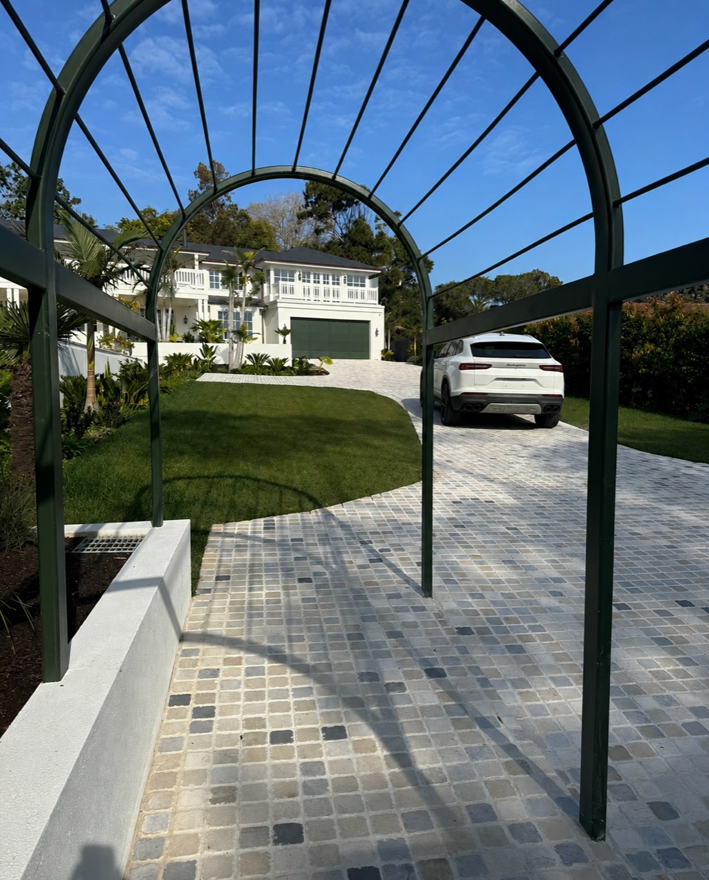 Light cobblestone driveway framed by a deep green arched garden structure at a Mt Martha residence